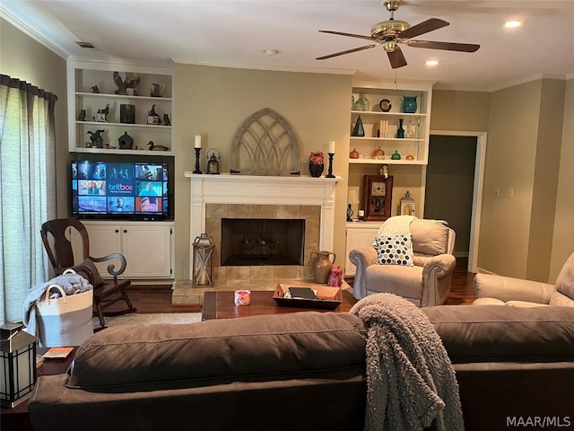 living room featuring a tile fireplace, built in shelves, ceiling fan, ornamental molding, and hardwood / wood-style flooring