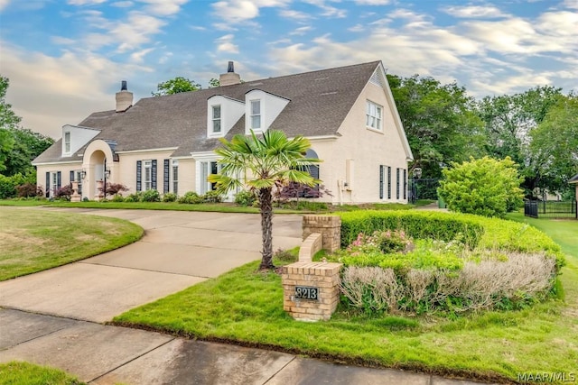 cape cod-style house with concrete driveway, a front lawn, and stucco siding