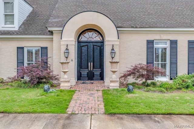 property entrance featuring a yard, brick siding, and roof with shingles