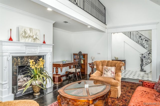 sitting room featuring visible vents, a tiled fireplace, dark wood-type flooring, a high ceiling, and crown molding