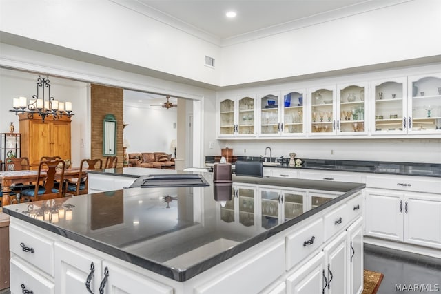 kitchen with brick wall, ceiling fan with notable chandelier, a center island, ornamental molding, and white cabinets