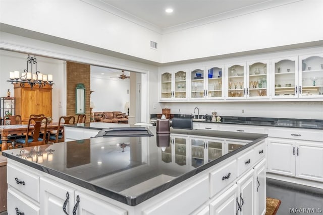 kitchen featuring white cabinets, dark countertops, a kitchen island, glass insert cabinets, and crown molding