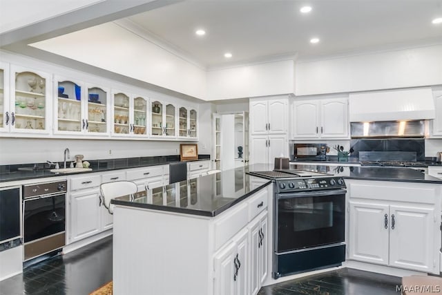 kitchen featuring dark countertops, glass insert cabinets, white cabinets, premium range hood, and black appliances