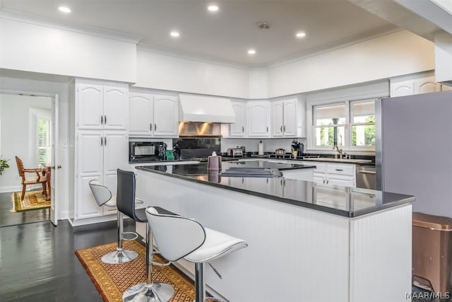 kitchen with black microwave, dark countertops, crown molding, wall chimney range hood, and white cabinetry