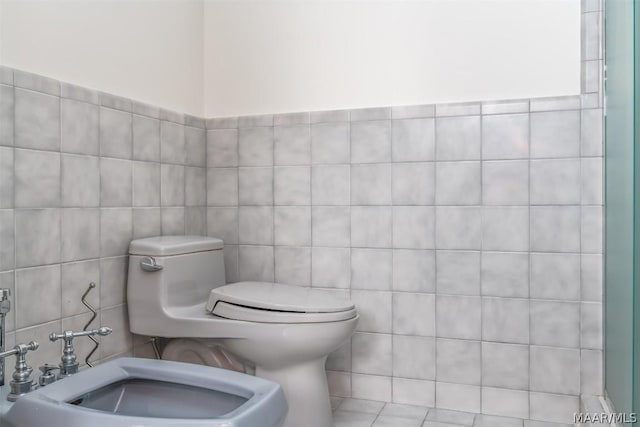 bathroom with a bidet, a sink, tile walls, and toilet