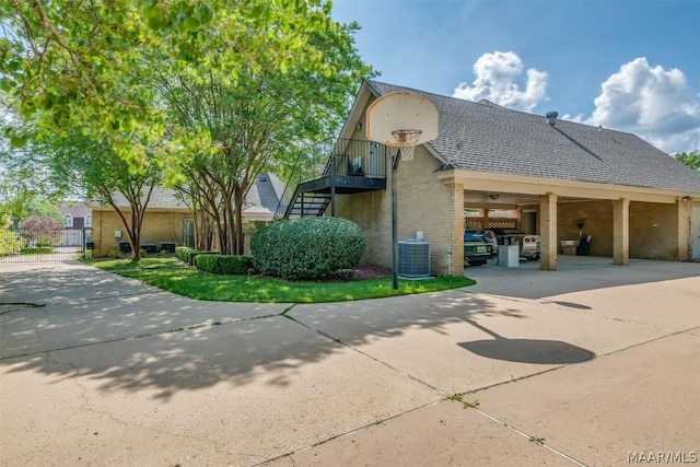 exterior space featuring brick siding, a shingled roof, central AC unit, driveway, and stairs