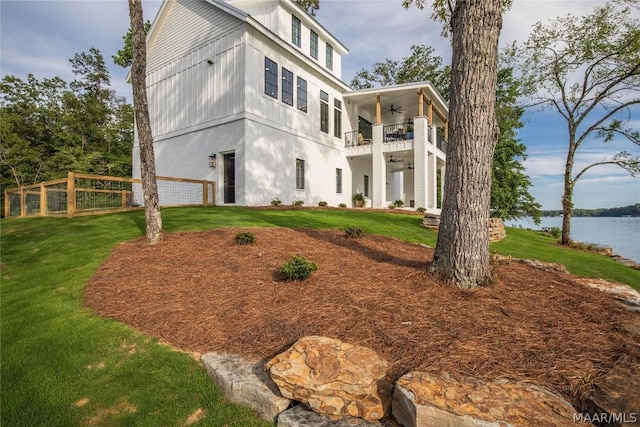 view of front of house featuring ceiling fan, a front lawn, a balcony, and a water view