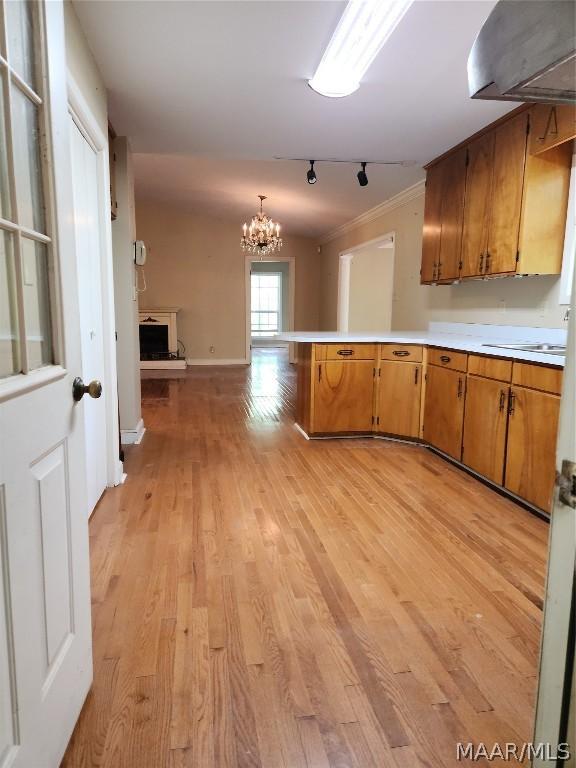 kitchen with kitchen peninsula, light wood-type flooring, rail lighting, ornamental molding, and a chandelier