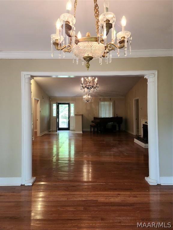 unfurnished living room with a notable chandelier, dark hardwood / wood-style flooring, and crown molding