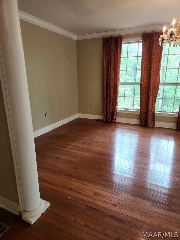 empty room with dark wood-type flooring, ornate columns, ornamental molding, and an inviting chandelier