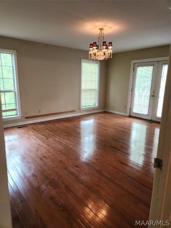 unfurnished room featuring wood-type flooring, plenty of natural light, and a chandelier