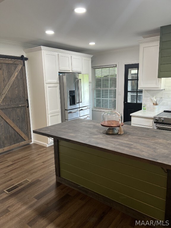 kitchen featuring tasteful backsplash, dark hardwood / wood-style floors, white cabinets, a barn door, and stainless steel appliances