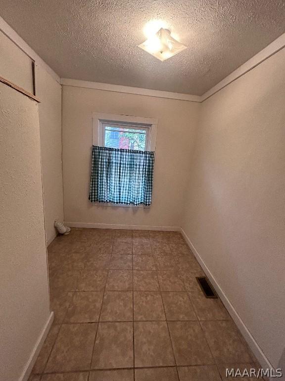 spare room with baseboards, visible vents, a textured ceiling, and tile patterned floors