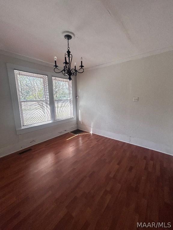 unfurnished dining area featuring an inviting chandelier, baseboards, ornamental molding, and wood finished floors