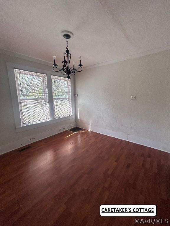 unfurnished dining area with baseboards, ornamental molding, wood finished floors, and an inviting chandelier