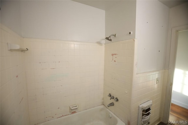 bathroom with tile walls, heating unit, and tiled shower / bath