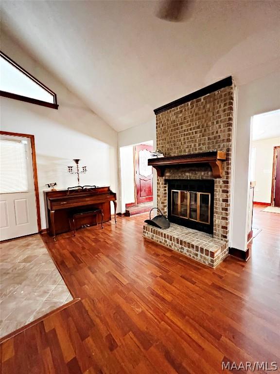 living room featuring wood-type flooring, lofted ceiling, and a brick fireplace