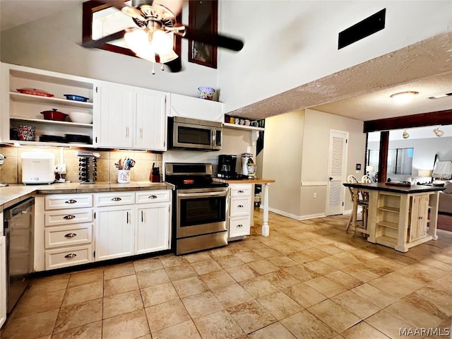 kitchen with tasteful backsplash, stainless steel appliances, ceiling fan, a high ceiling, and white cabinetry