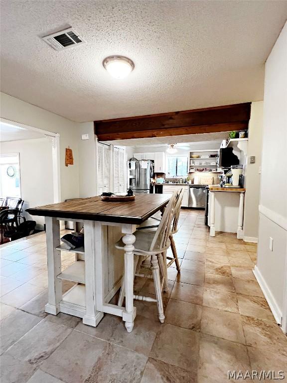 kitchen with a textured ceiling, butcher block counters, stainless steel appliances, and a breakfast bar area