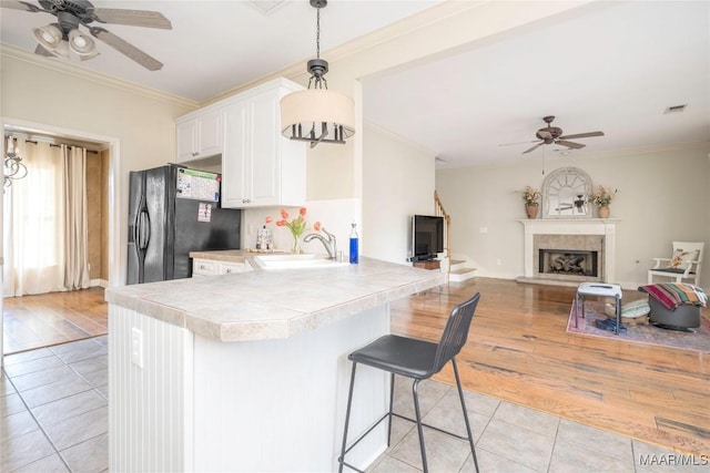 kitchen with a kitchen breakfast bar, kitchen peninsula, light hardwood / wood-style floors, black fridge with ice dispenser, and white cabinets