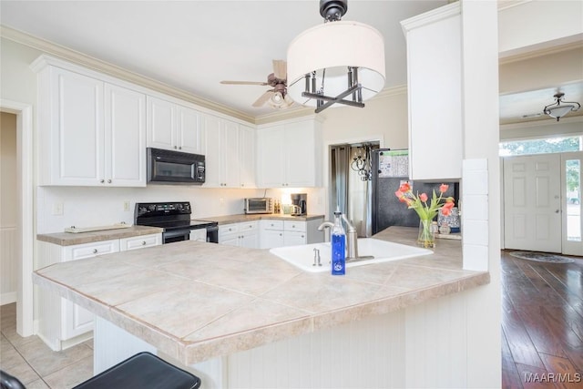 kitchen featuring black appliances, white cabinets, hanging light fixtures, hardwood / wood-style flooring, and kitchen peninsula