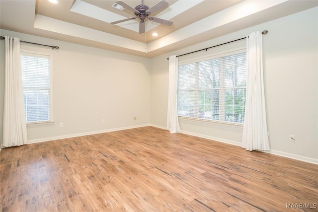 spare room featuring ceiling fan, light wood-type flooring, a wealth of natural light, and a tray ceiling