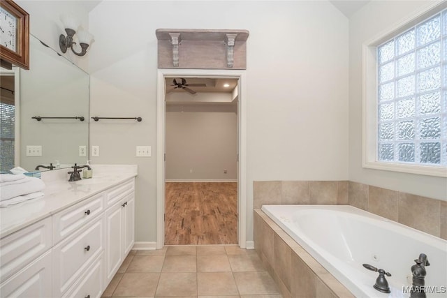 bathroom featuring tile patterned flooring, ceiling fan, a relaxing tiled tub, and vanity