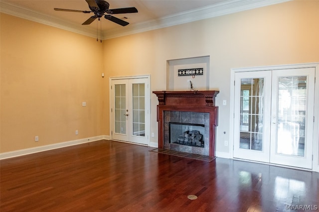 unfurnished living room with ceiling fan, french doors, dark hardwood / wood-style floors, a tiled fireplace, and ornamental molding