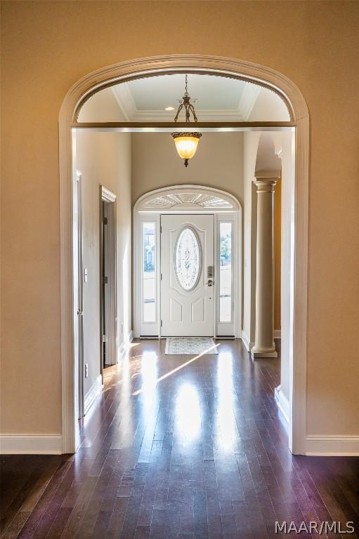 entryway with ornate columns, crown molding, and dark wood-type flooring