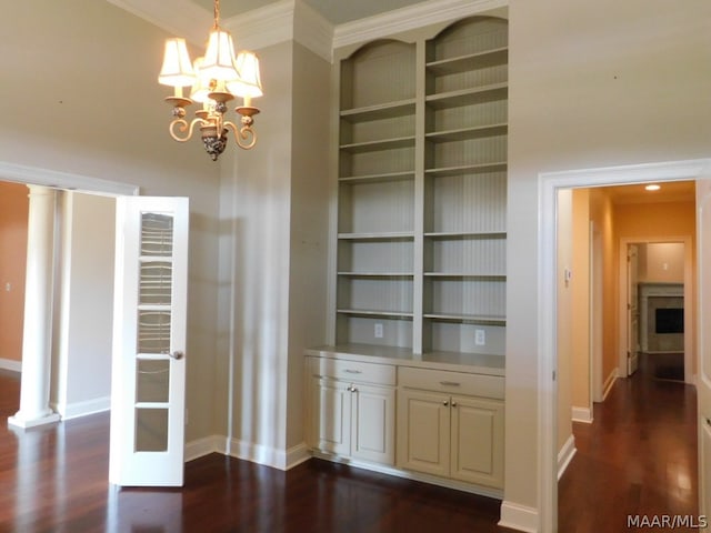 unfurnished dining area featuring a chandelier, dark hardwood / wood-style floors, ornate columns, and built in features