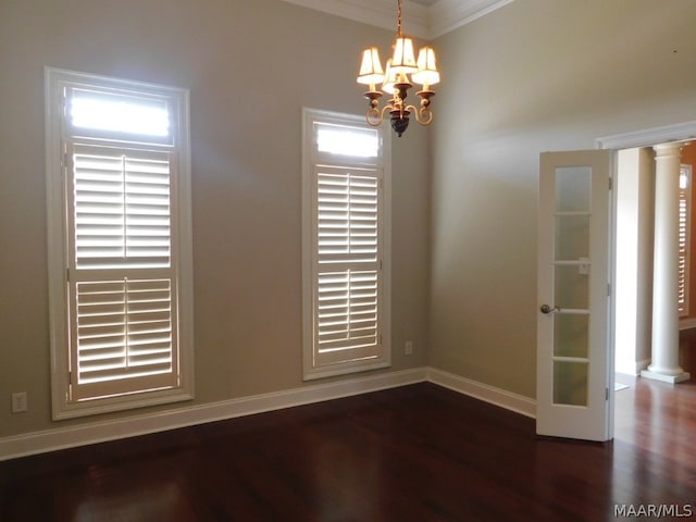 spare room with decorative columns, dark hardwood / wood-style flooring, ornamental molding, and an inviting chandelier