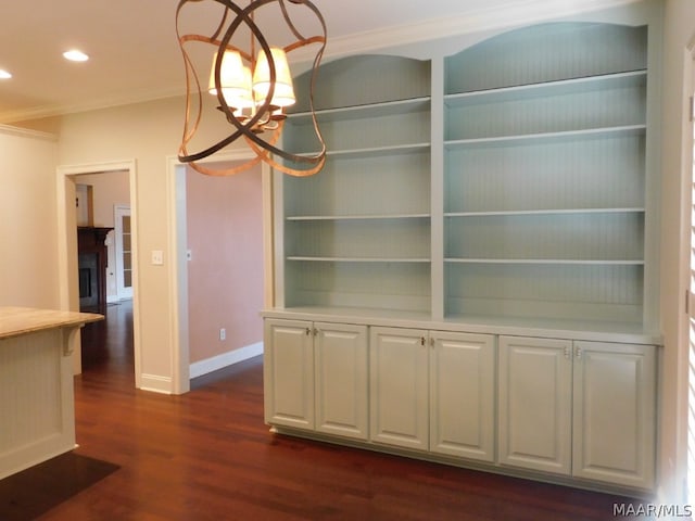 unfurnished dining area with built in shelves, dark hardwood / wood-style flooring, an inviting chandelier, and ornamental molding