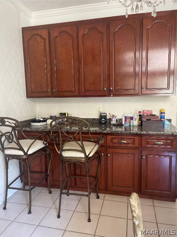 kitchen with dark stone countertops, light tile patterned floors, ornamental molding, and a breakfast bar area