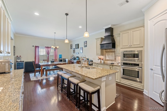 kitchen with cream cabinets, sink, appliances with stainless steel finishes, decorative light fixtures, and custom range hood