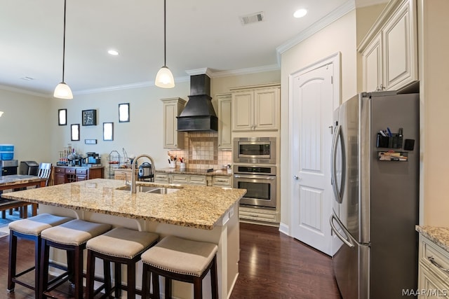 kitchen featuring light stone countertops, custom range hood, stainless steel appliances, cream cabinets, and hanging light fixtures