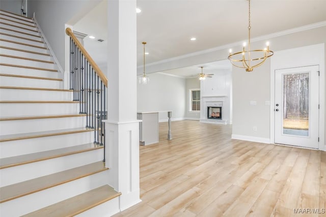 staircase with a warm lit fireplace, a ceiling fan, ornamental molding, wood finished floors, and recessed lighting