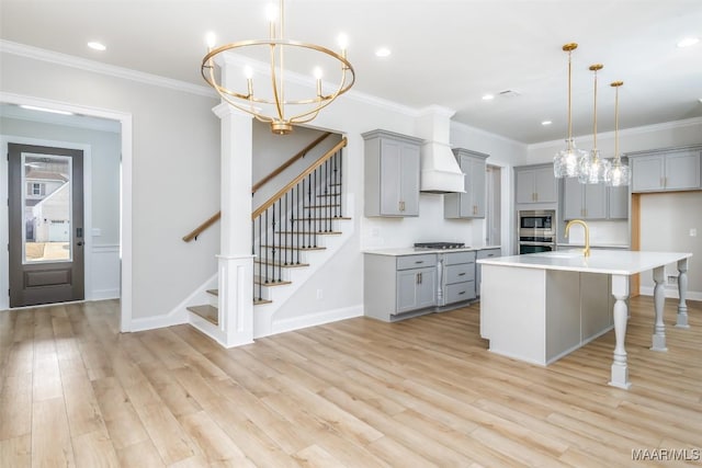 kitchen featuring a center island with sink, light countertops, hanging light fixtures, and gray cabinetry