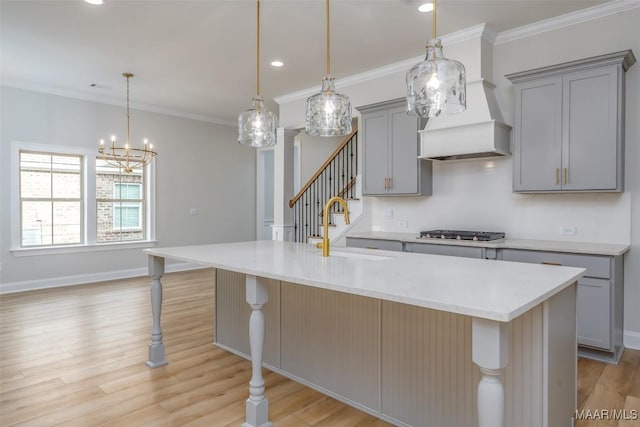 kitchen featuring stainless steel gas stovetop, a kitchen island with sink, a sink, and hanging light fixtures