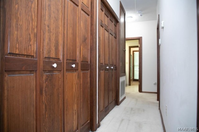 hallway featuring baseboards, visible vents, attic access, and light colored carpet