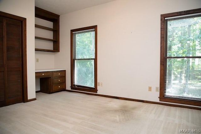 unfurnished bedroom with light carpet, multiple windows, baseboards, and built in study area