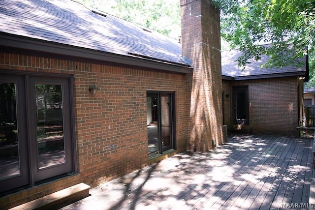 exterior space with a deck, a shingled roof, a chimney, and brick siding