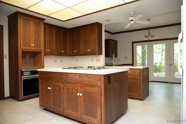 kitchen featuring wall oven, white stovetop, ornamental molding, a center island, and light floors