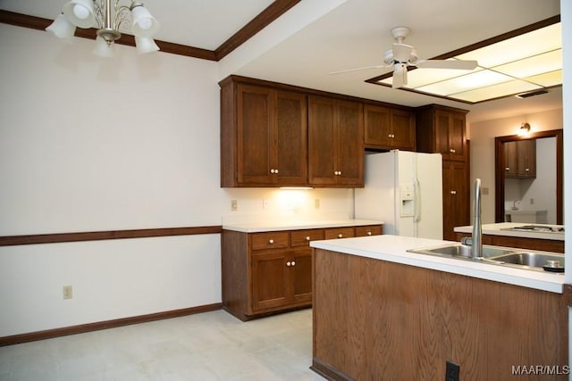 kitchen with light countertops, a sink, white fridge with ice dispenser, baseboards, and ceiling fan with notable chandelier