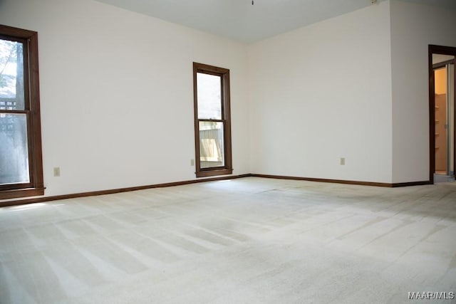 spare room featuring light carpet, plenty of natural light, and baseboards