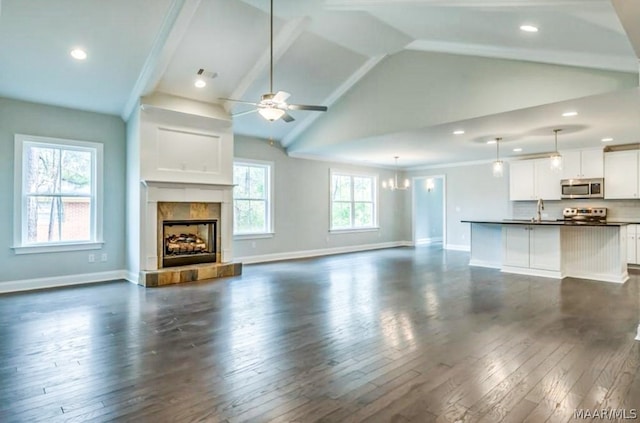 unfurnished living room with high vaulted ceiling, dark hardwood / wood-style floors, a tiled fireplace, and ceiling fan with notable chandelier