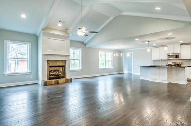 unfurnished living room with baseboards, a tile fireplace, vaulted ceiling, ceiling fan, and dark wood-style floors