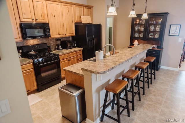 kitchen featuring a kitchen bar, sink, black appliances, and a center island with sink