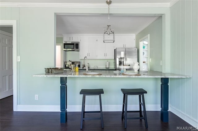 kitchen with white cabinetry, pendant lighting, a breakfast bar area, appliances with stainless steel finishes, and ornamental molding