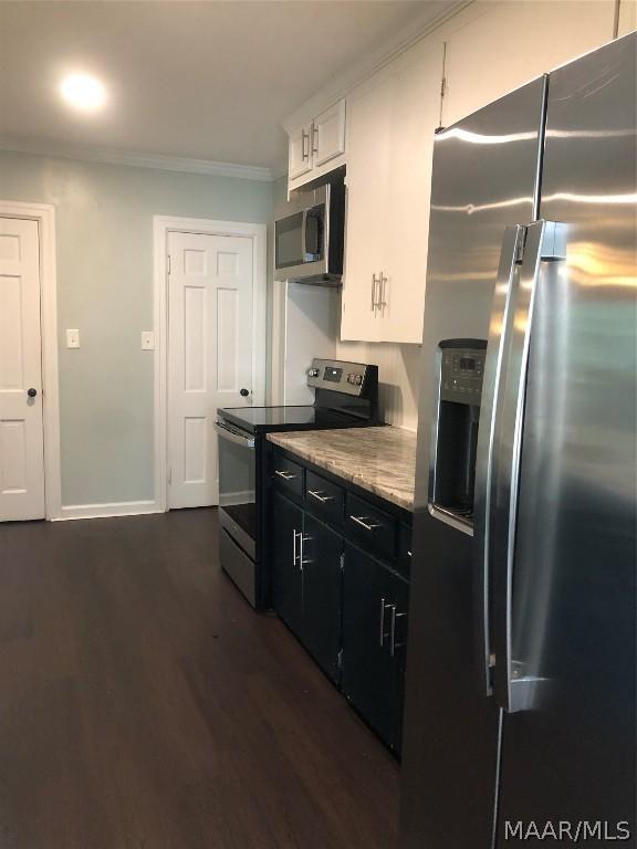 kitchen with dark hardwood / wood-style flooring, white cabinets, ornamental molding, and appliances with stainless steel finishes