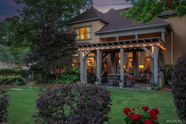 back house at dusk featuring a patio area, a pergola, and a yard